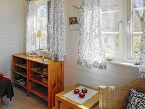 A room with a wooden bookshelf, a small table with red spherical objects, a wicker chair, and a window with floral curtains. - 6 Person Holiday Home in Gullspang (Gullspång)