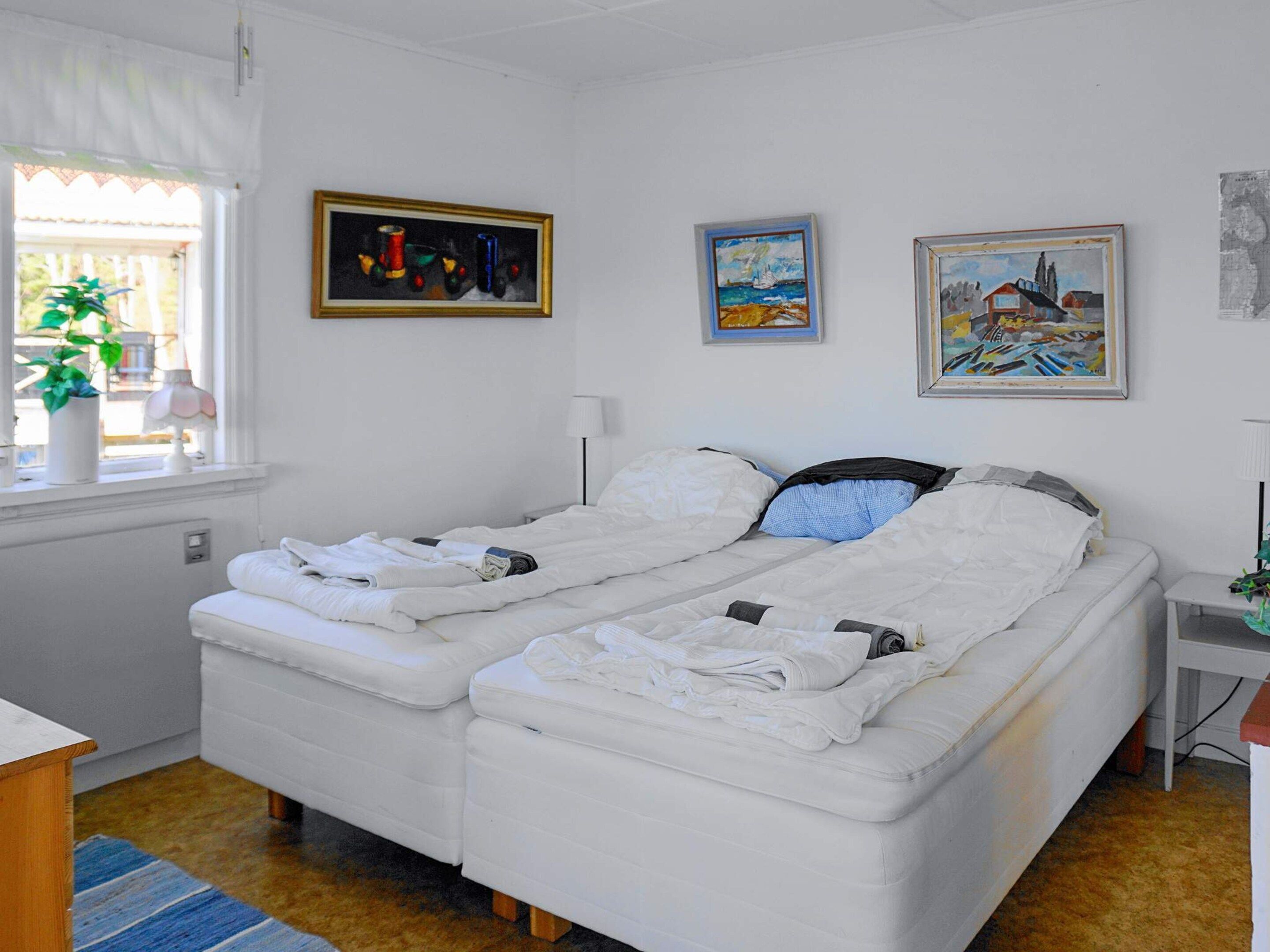 A room with a bed, a window with curtains, a lamp, and three paintings on the wall.