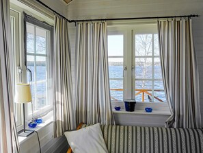 A bedroom with a view of a lake, a bed with striped bedding, a lamp, and curtains.