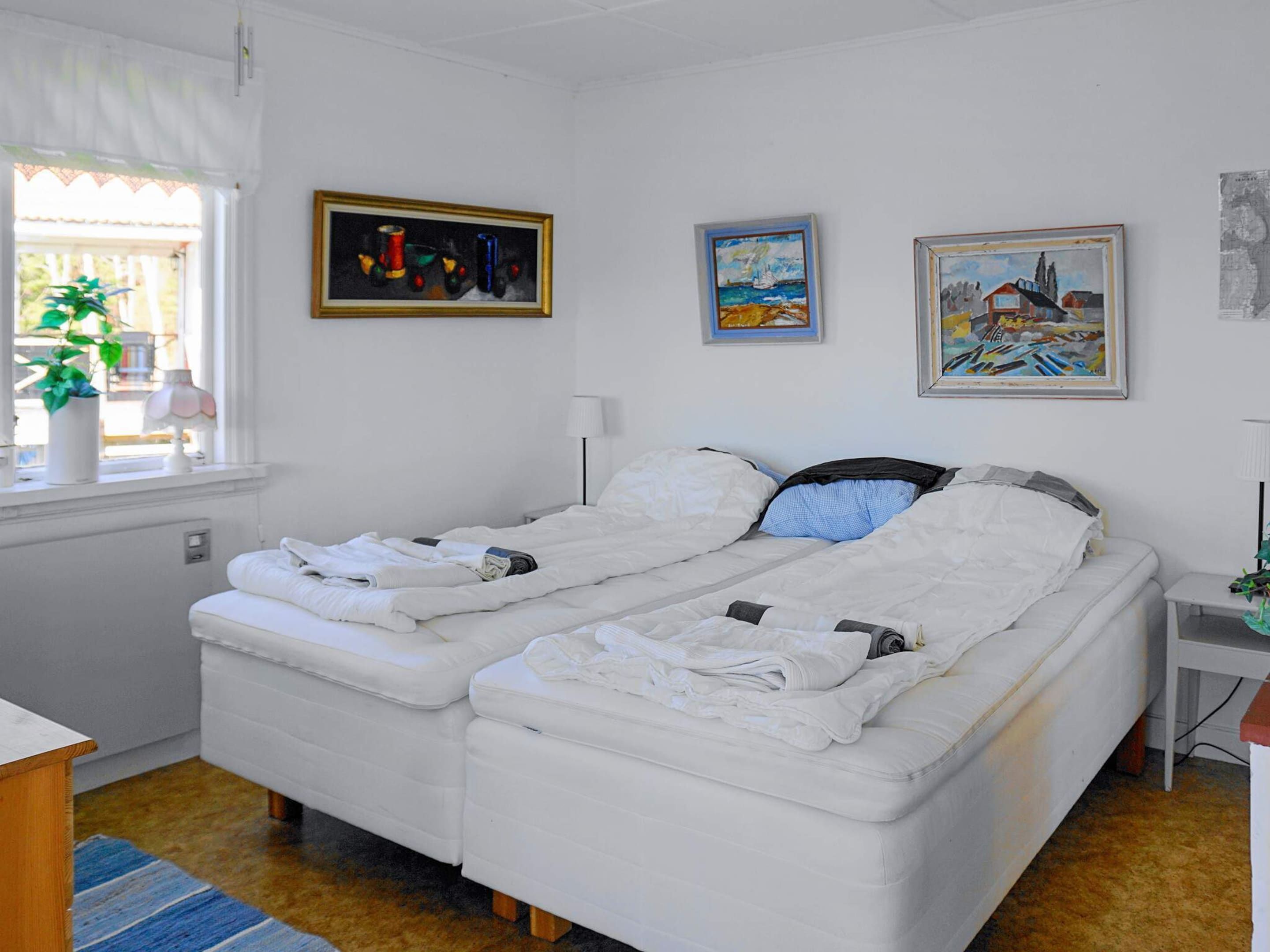 A double bed with white bedding, a bedside table with a lamp, and three paintings on the wall.