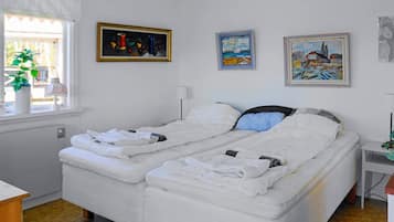 A double bed with white bedding, a bedside table with a lamp, and three paintings on the wall.