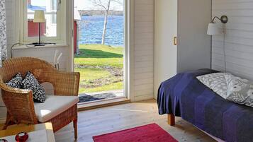 Un dormitorio con cama, una silla de mimbre, un tapete rojo y vistas a un lago.