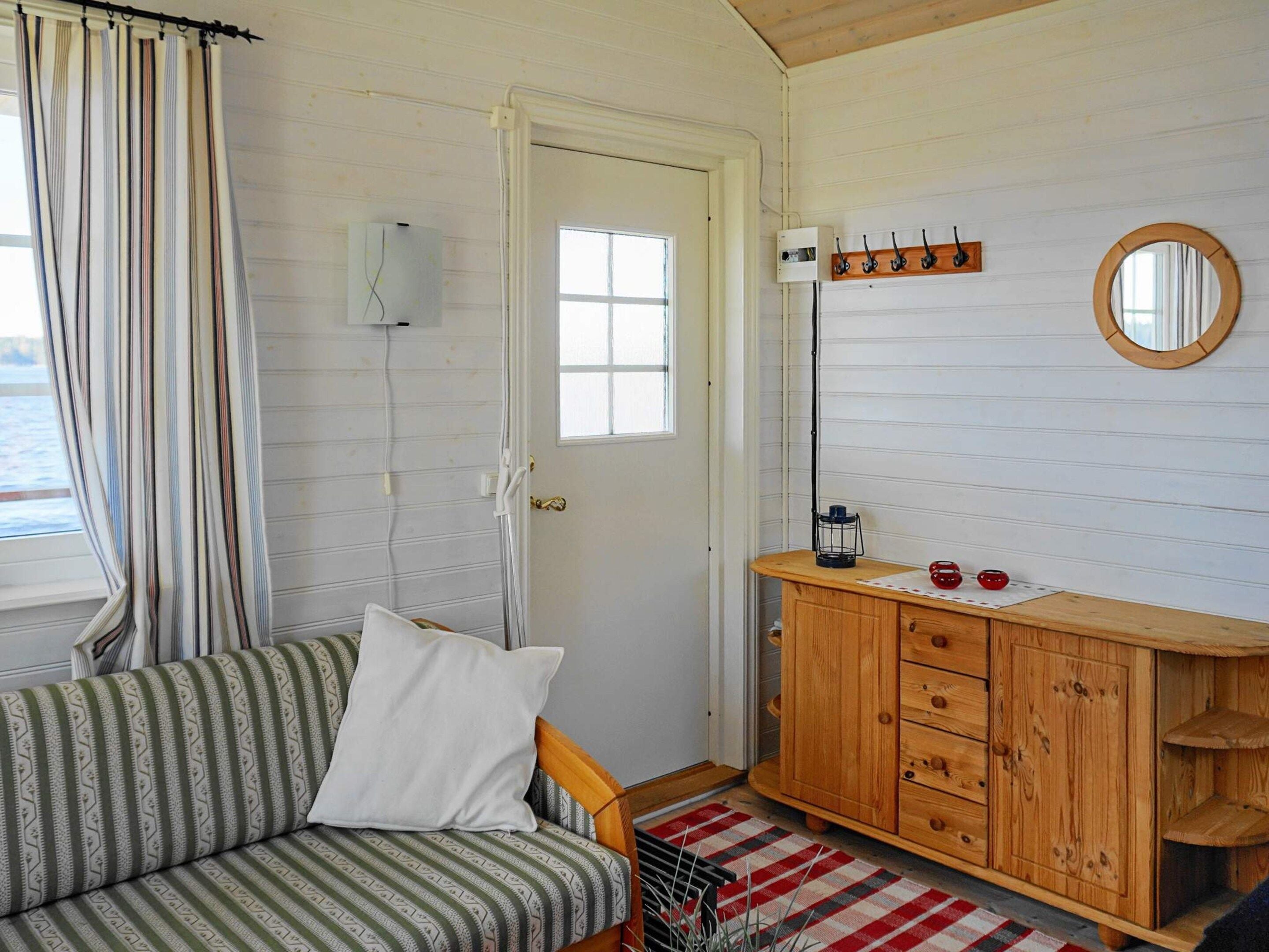 Una habitación con un sofá a rayas, un armario de madera, un espejo y un ventanal con cortinas.
