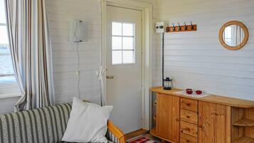 Una habitación con un sofá a rayas, un armario de madera, un espejo y un ventanal con cortinas.
