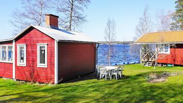 A red wooden house with a white door and windows, a small table with chairs, and a wooden deck.