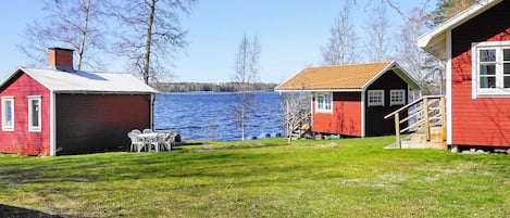 A lakeside cabin with a red exterior, a small deck, and a table with chairs.