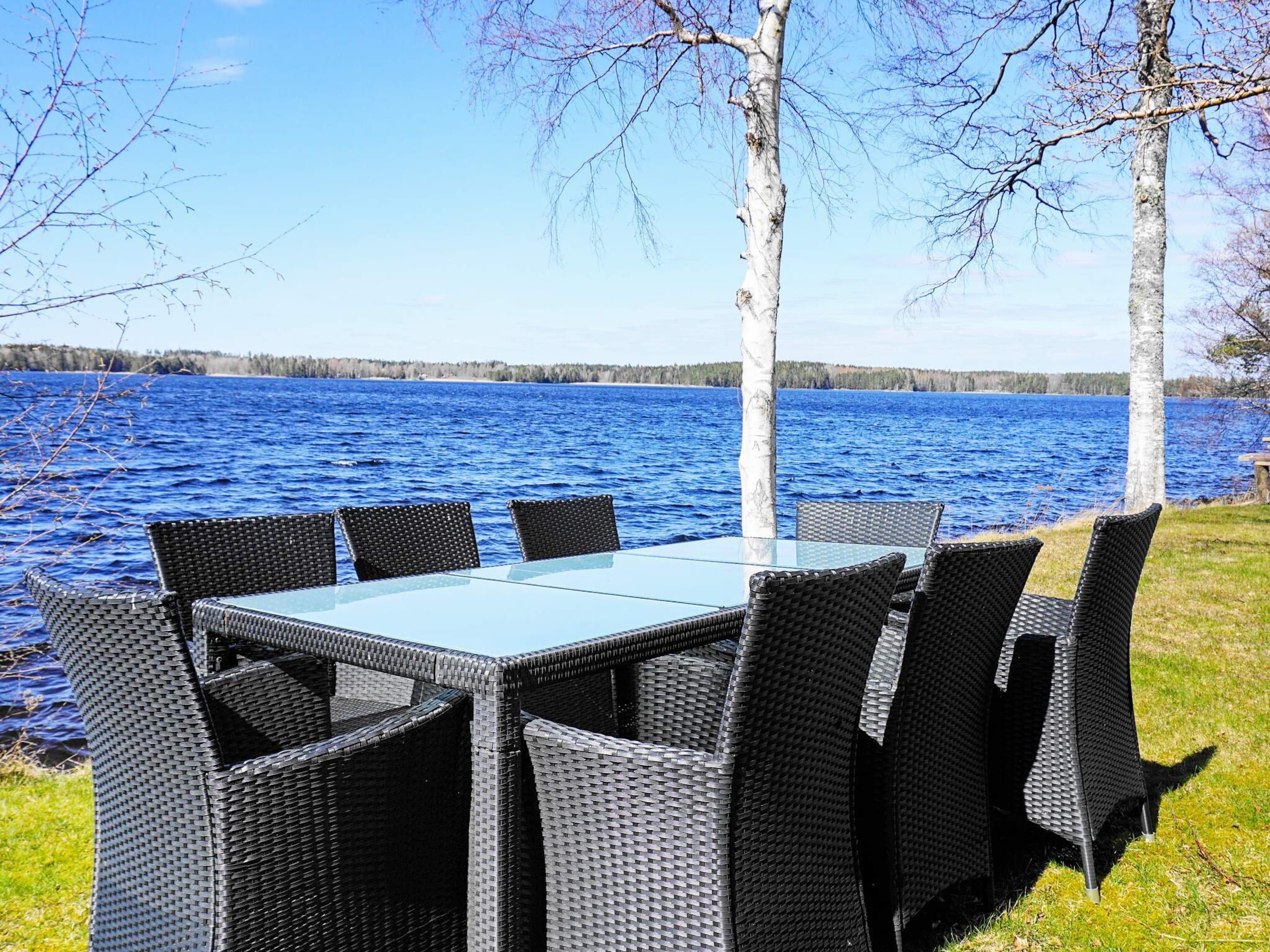 A table and chairs set up by a lakeside with birch trees.
