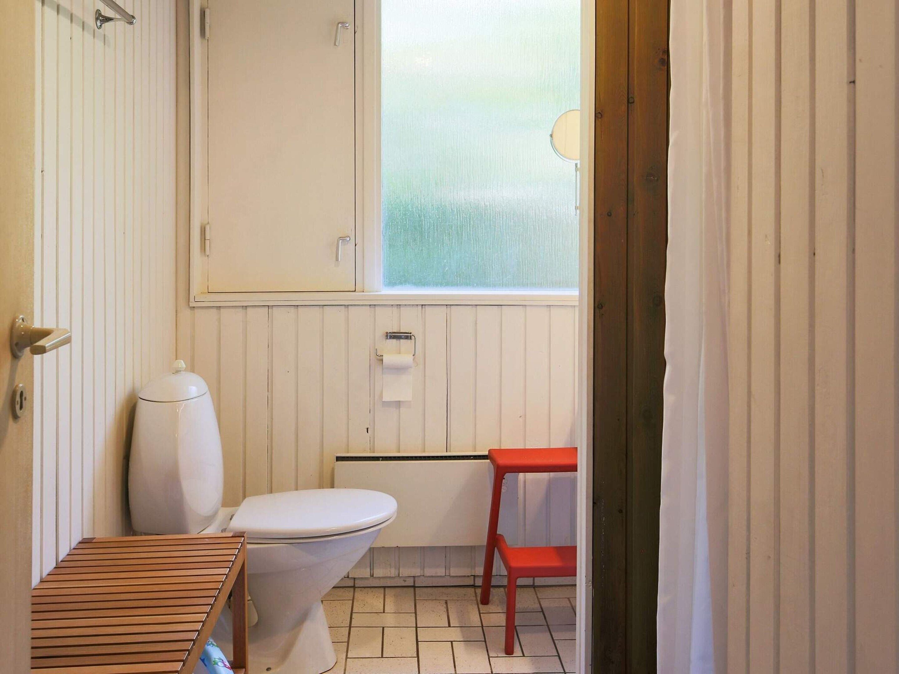 Een kleine, praktische badkamer met toilet, wastafel en raam.