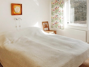 A bedroom with a bed, a chair, a window with curtains, and a wall-mounted picture.