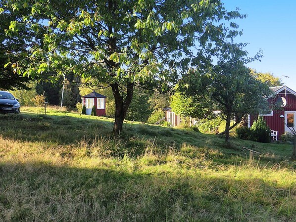 A rural landscape with a red barn, a small wooden structure, and a tree.