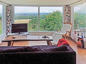Ein Zimmer mit großem Fenster, Fernseher, Tisch mit Gewichten, Stuhl und einer Couch.