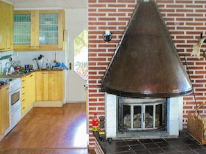 Een keuken met houten kasten en een fornuis, een met een metalen afzuigkap omringde, met bakstenen schoorsteen, en een raam met luiken.