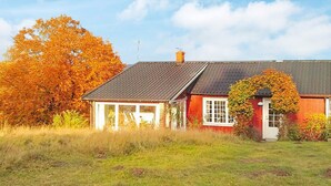 Une maison rouge avec un toit en pente, un petit porche et, au fond, un grand arbre aux feuilles orange.