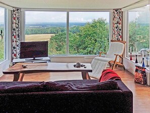 A room with a large window, a television, a table with a chair, and a sofa.