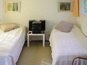 A room with two single beds, a small table with a speaker, and a window with curtains.
