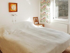 A bedroom with a bed, a chair, a window with curtains, and a wall-mounted picture.