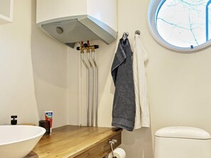 A bathroom with a wooden vanity, a white sink, a toilet, and a window with a view of bare trees. - 4 Person Holiday Home in Grisslehamn (Grisslehamn)