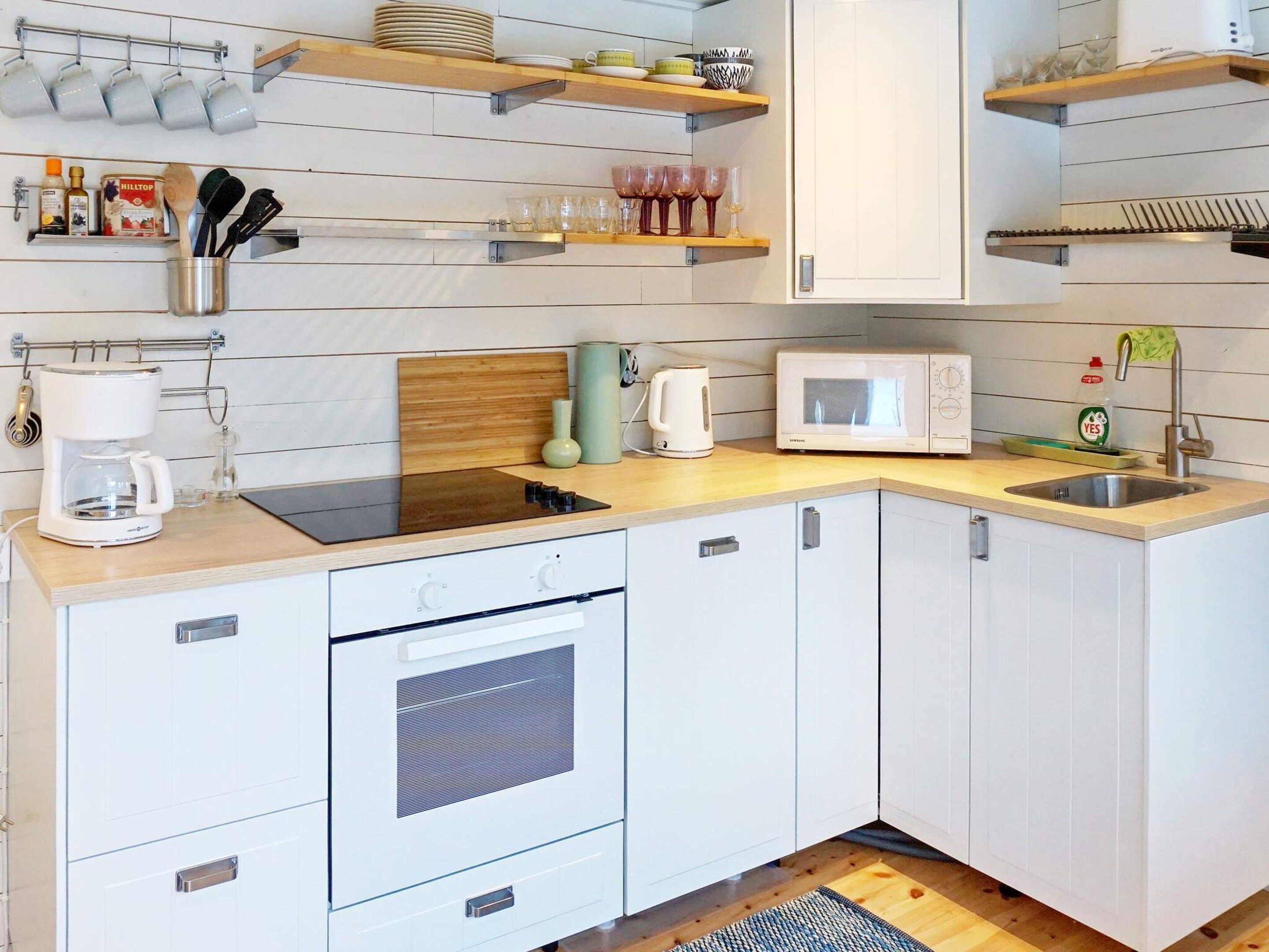 A modern kitchen with white cabinets, a microwave, a coffee maker, and various utensils on shelves.