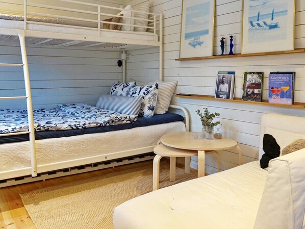 Un lit superposé avec une couvre-lit à motifs, une petite table ronde avec un vase et un canapé avec un coussin.