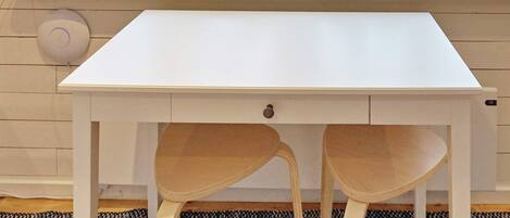 A white desk with two chairs, a window with a view of trees, and various decorative items on the windowsill.