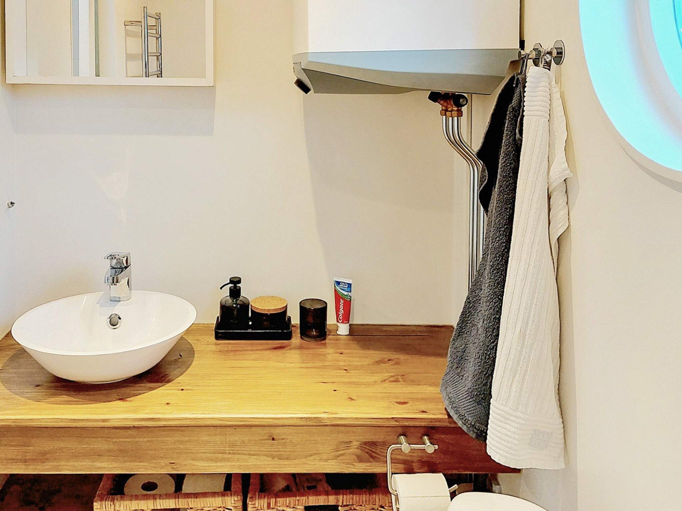 A bathroom with a white sink, a wooden countertop, a soap dispenser, a toothbrush holder, and a towel rack with a towel.