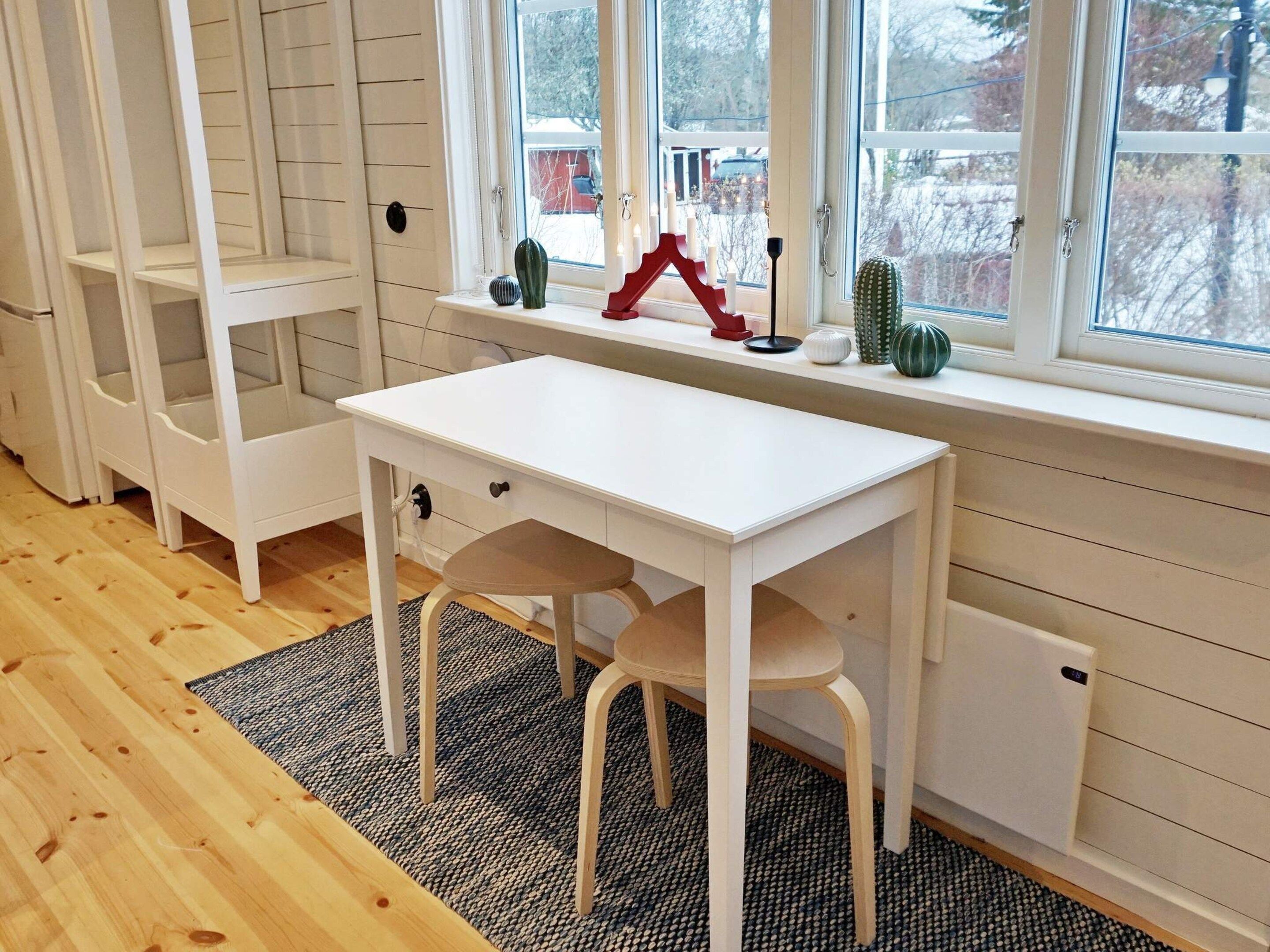 A white desk with a chair, a window with a view of trees, and a shelf with decorative items.