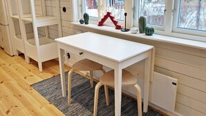A white desk with a chair, a window with a view of trees, and a shelf with decorative items. - 4 Person Holiday Home in Grisslehamn (Grisslehamn)