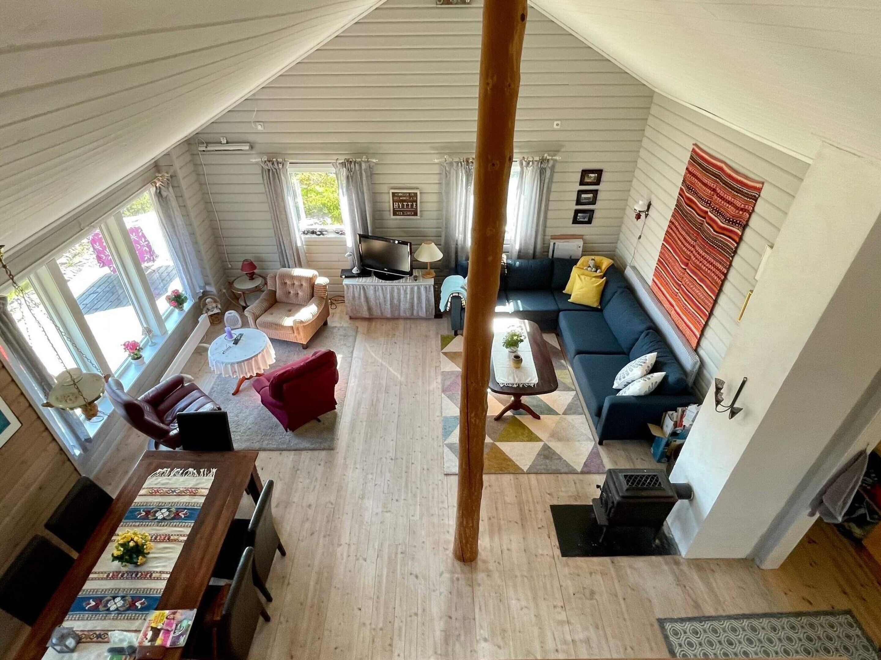 A spacious living room with a large sofa, a dining table, and a TV. There are curtains on the windows and a fireplace.