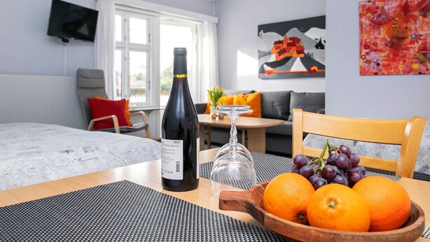Ein Hotelzimmer mit einem Bett, einem Esstisch, einer Weinflasche, einer Obstschale und einem Bild an der Wand.