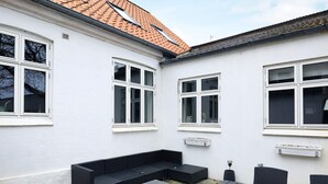 A white building with a tiled roof, a black outdoor seating area with a table, and multiple windows.