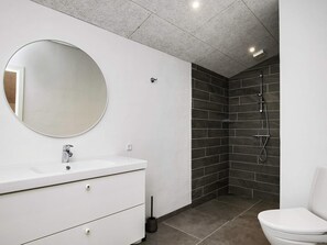 A modern bathroom with a white vanity, a round mirror, a shower with dark tiles, and a white toilet.