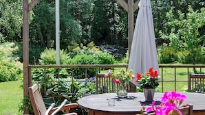 Une table en bois pour l’extérieur, avec des chaises, entourée de plantes et de fleurs en pot.