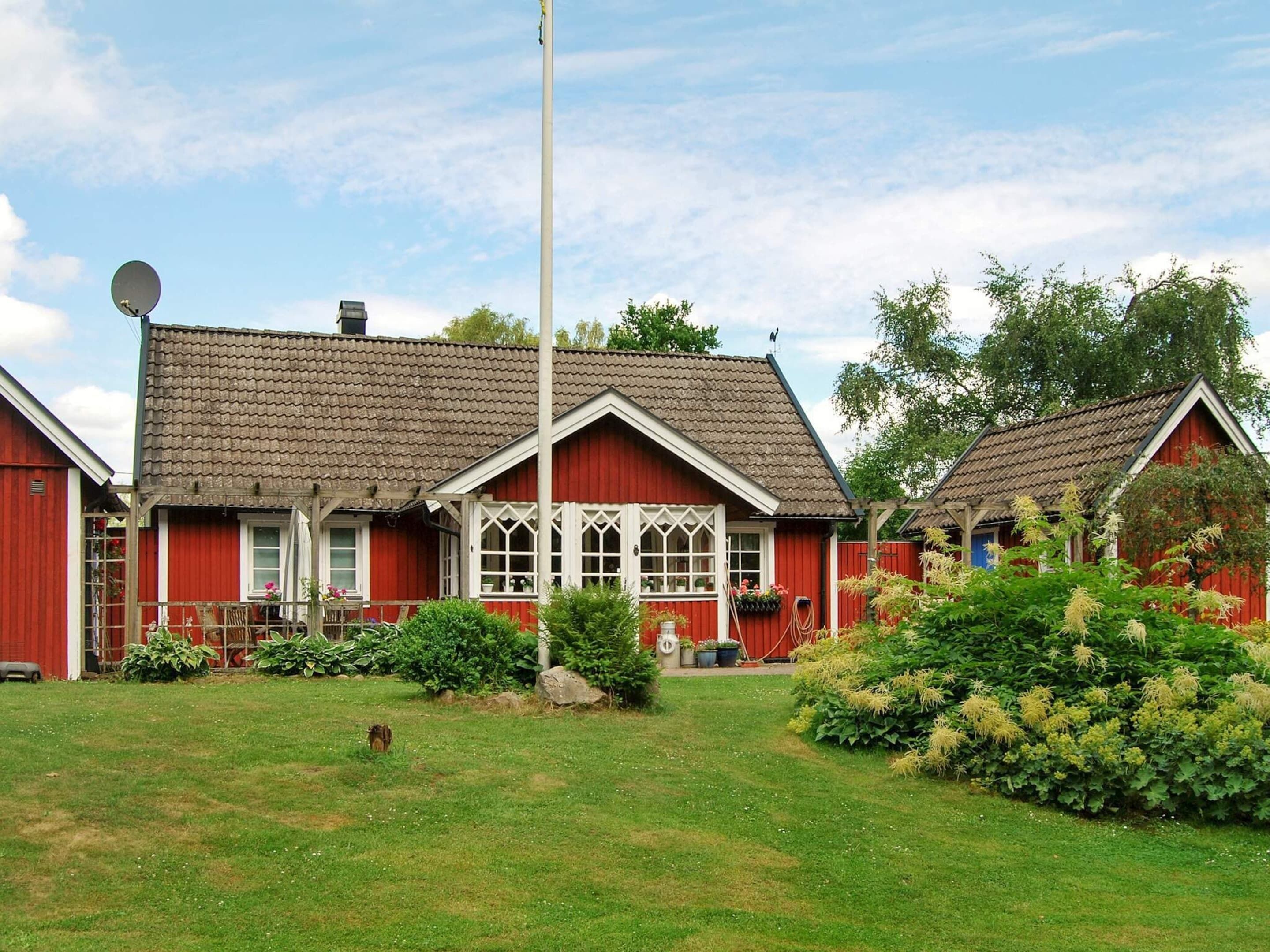 Ein rotes Holzhaus mit Ziegeldach, Satellitenschüssel und gepflegtem Garten.