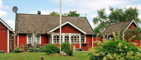 Ein rotes Holzhaus mit Ziegeldach, Satellitenschüssel und gepflegtem Garten.