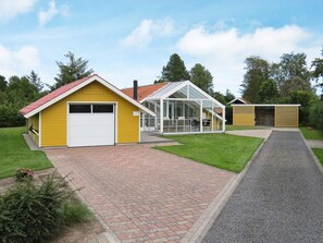 A yellow building with a garage, a glass conservatory, and a wooden shed. - 6 Person Holiday Home in Hals (Hals)