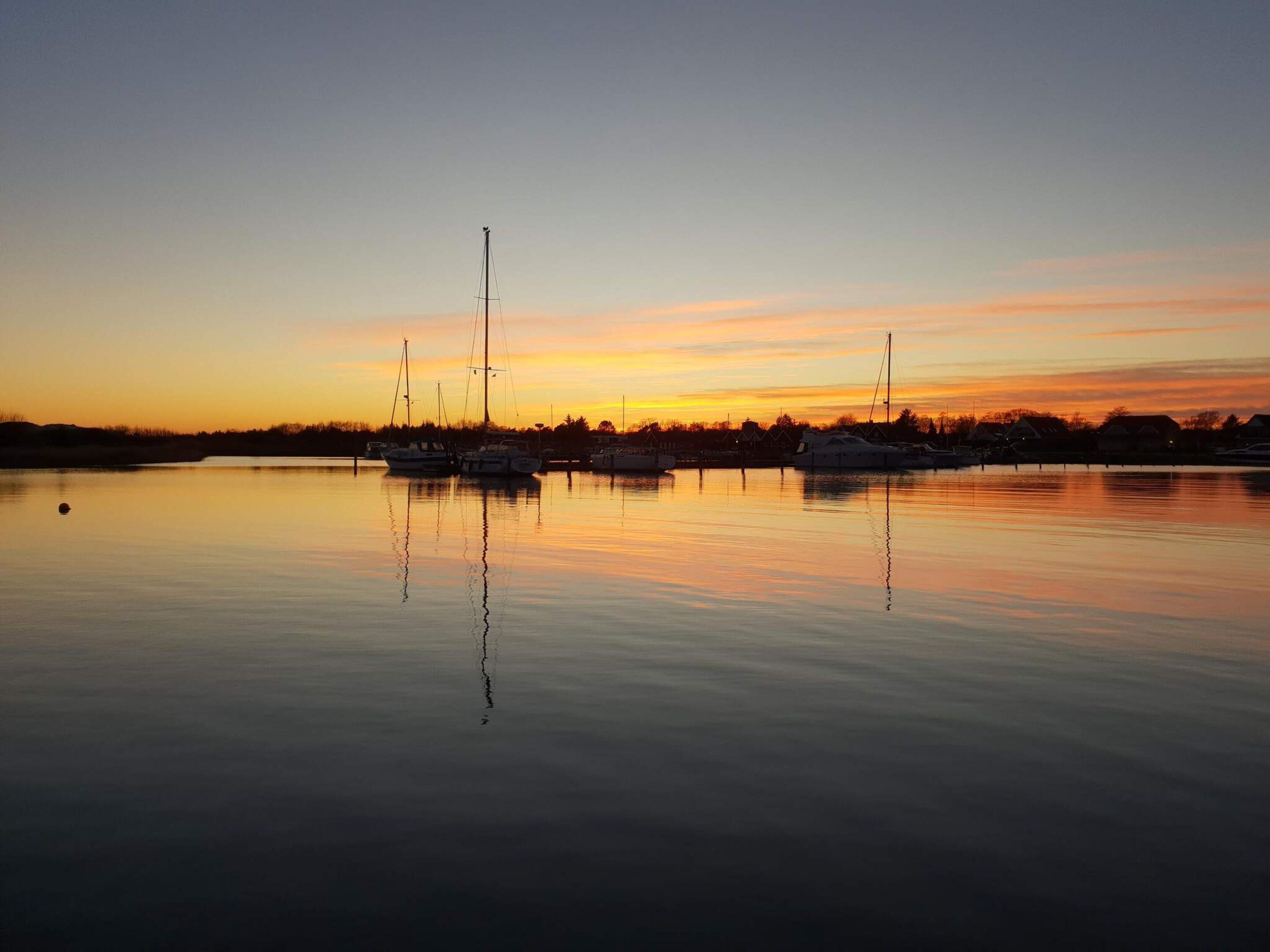 A calm body of water reflecting boats and a sunset sky.