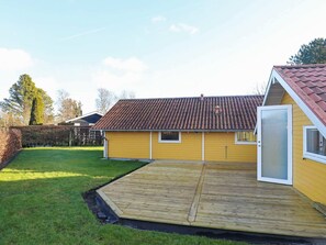 Un bâtiment jaune avec un toit recouvert de tuiles rouges, une terrasse en bois et une porte.