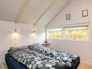 A bedroom with a bed, two wall-mounted lamps, a window with blinds, and a small shelf with a cactus.
