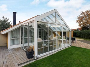 A modern house with a large glass conservatory, wooden deck, and a well-maintained lawn.