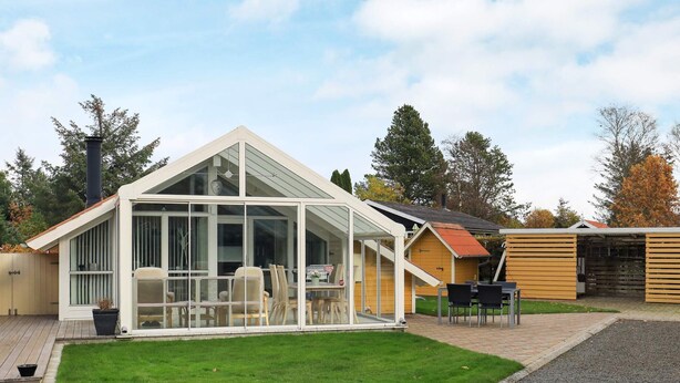 A modern house with a glass conservatory, a wooden deck, and a well-maintained lawn. - 4 Star Holiday Home in Hals (Hals)