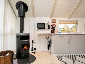 A modern kitchen with a wood-burning stove, a microwave, and a window with a view of trees.