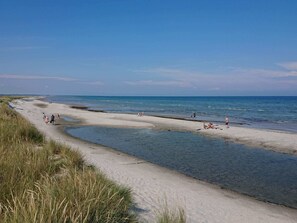 A beach with clear skies, a sandy shore, and people enjoying the water.