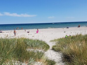 Ein sandiger Strand mit Menschen und blauem Himmel.
