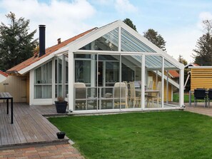 A modern house with a glass conservatory, a wooden deck, and a well-maintained lawn.