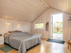 A bedroom with a bed, wooden walls, a window, and a door leading outside.