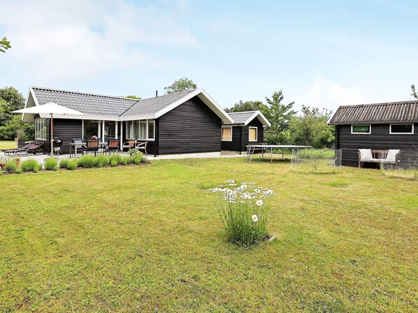 A modern house with a covered patio, a lawn, and a small garden.