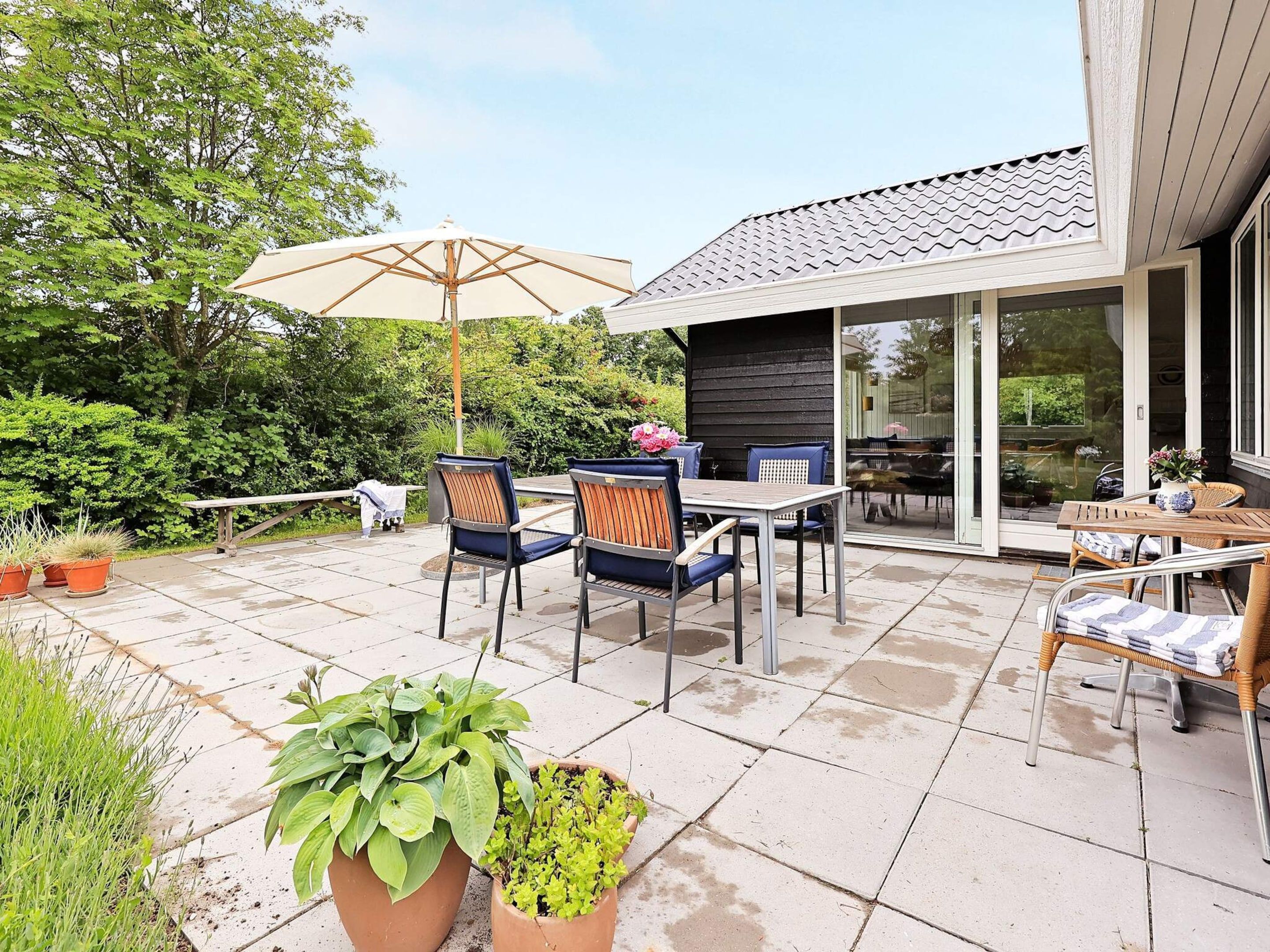 An outdoor patio with a table and chairs, surrounded by potted plants.