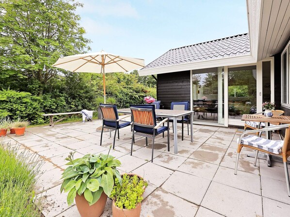 An outdoor patio with a table and chairs, surrounded by potted plants.