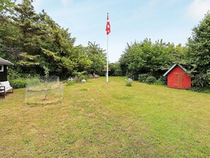 A grassy area with a flagpole, a red shed, and a bench. - 4 Star Holiday Home in Karrebaeksminde (Karrebæksminde)