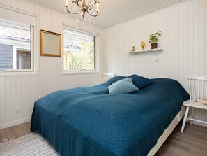 A bedroom with a bed, a chandelier, a window, a mirror, and a shelf with a plant.